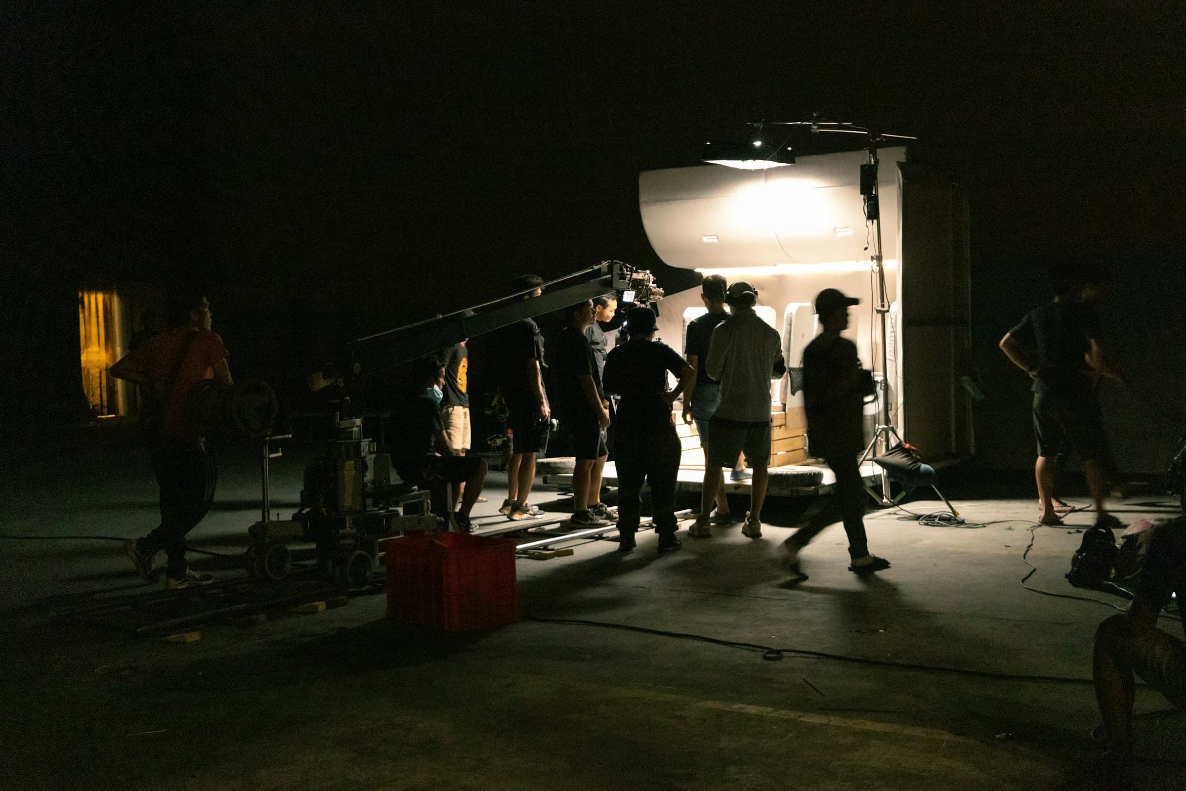 Film crew operating a camera crane and studio lighting on a dark commercial production set
